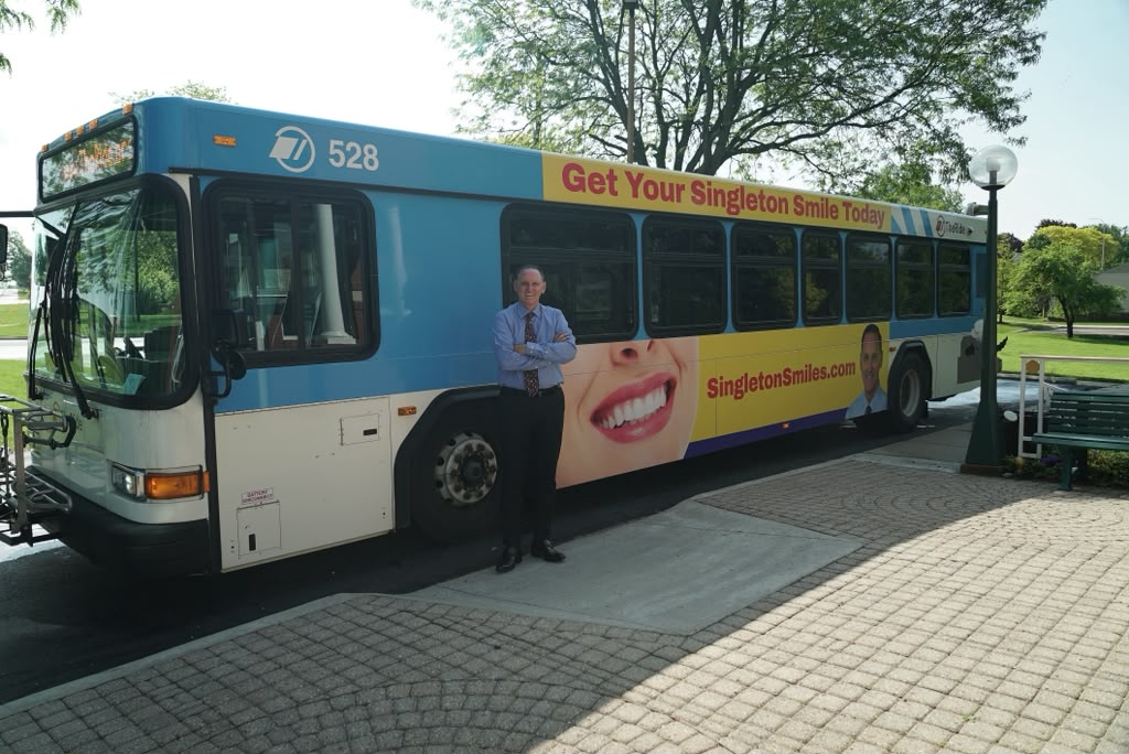Dr. Michael Singleton standing in front of the Singleton Smiles branded city bus in Saline, Michigan